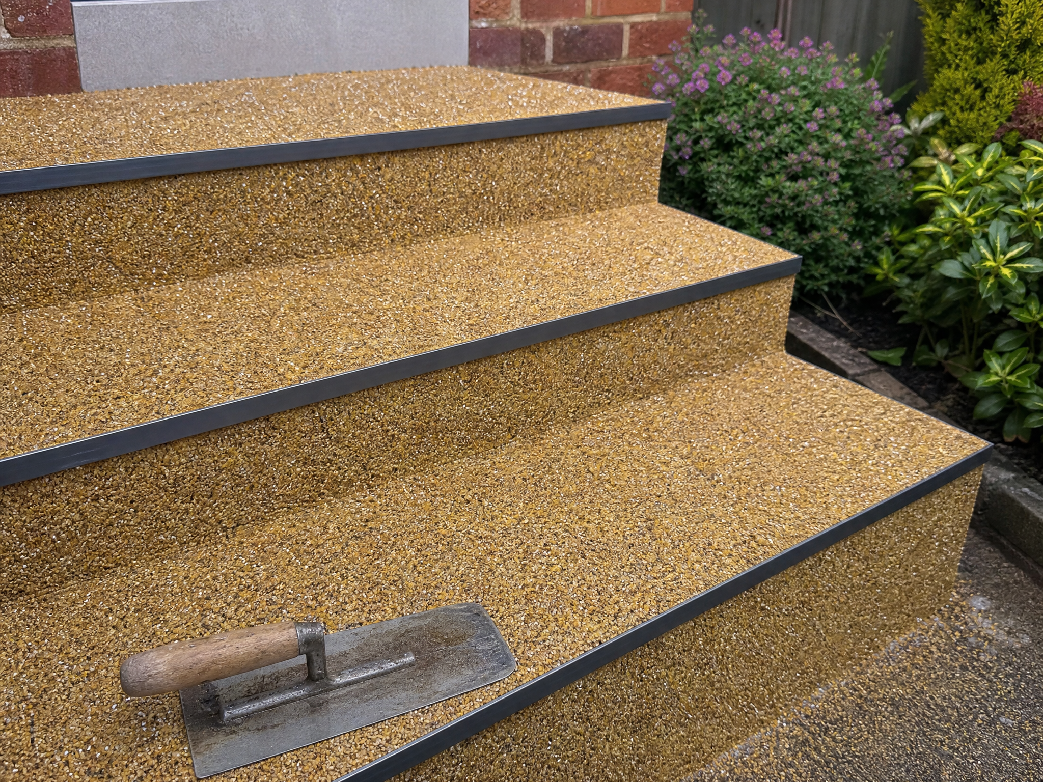 Golden resin bound garden steps with dark edge strips beside a red-brick house